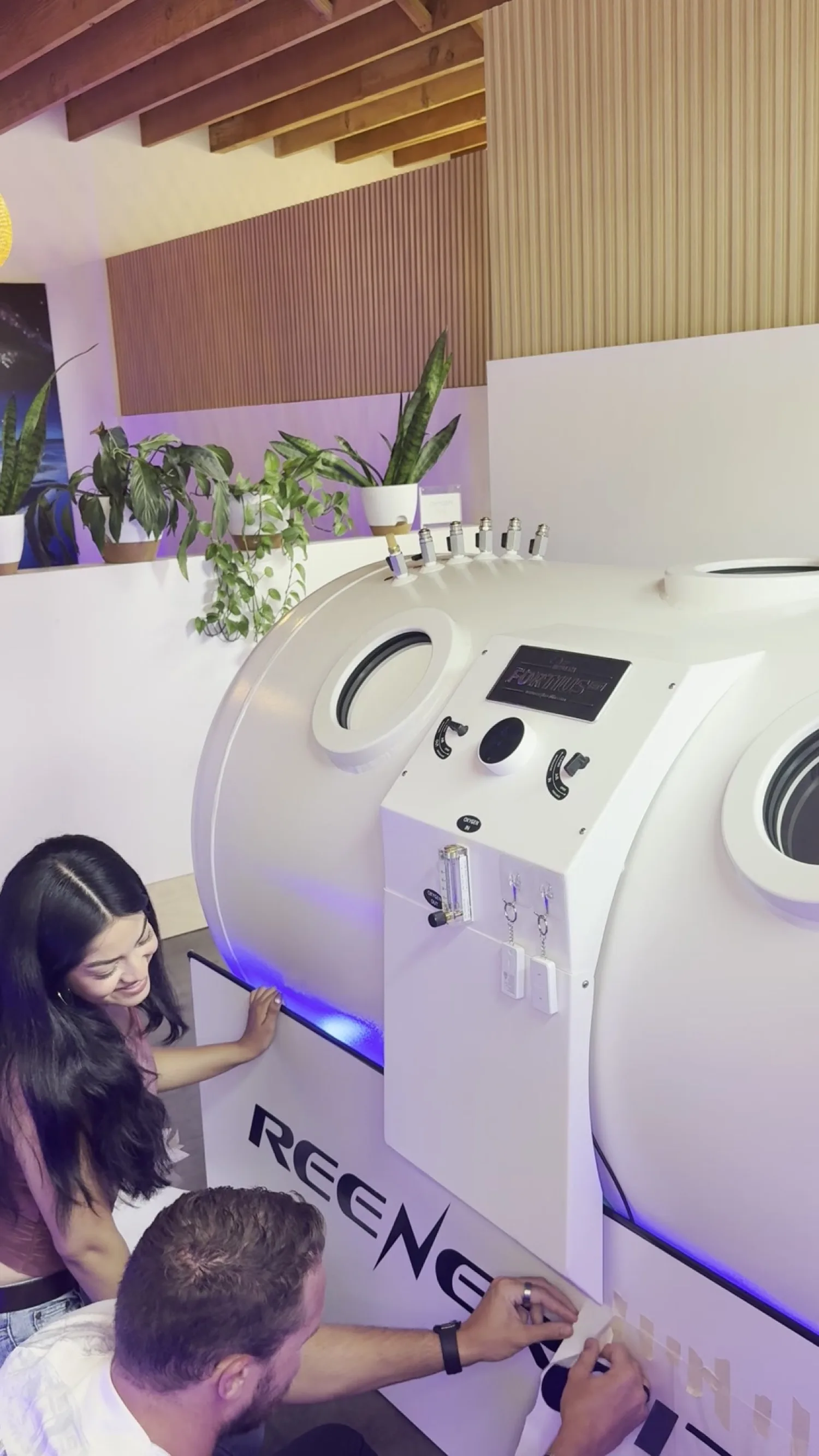 A smiling guest with her hand on the branded Fortius 2.0 ATA hard-shell chamber at the ReEnergized Long Beach studio